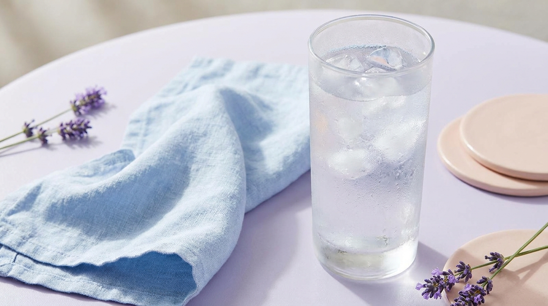 Frosted glass of iced water and a cooling cloth on a lilac surface